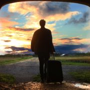 guy with suitcase walking away at sunset