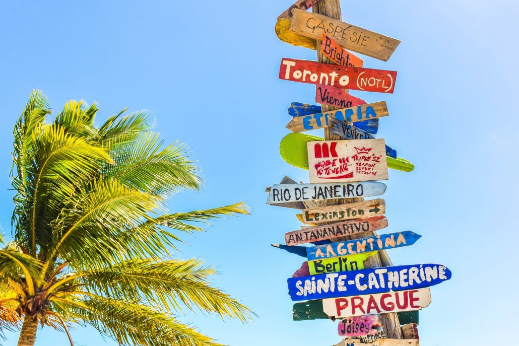 sign with locations to travel to and palm tree